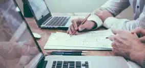 person holding pencil near laptop computer